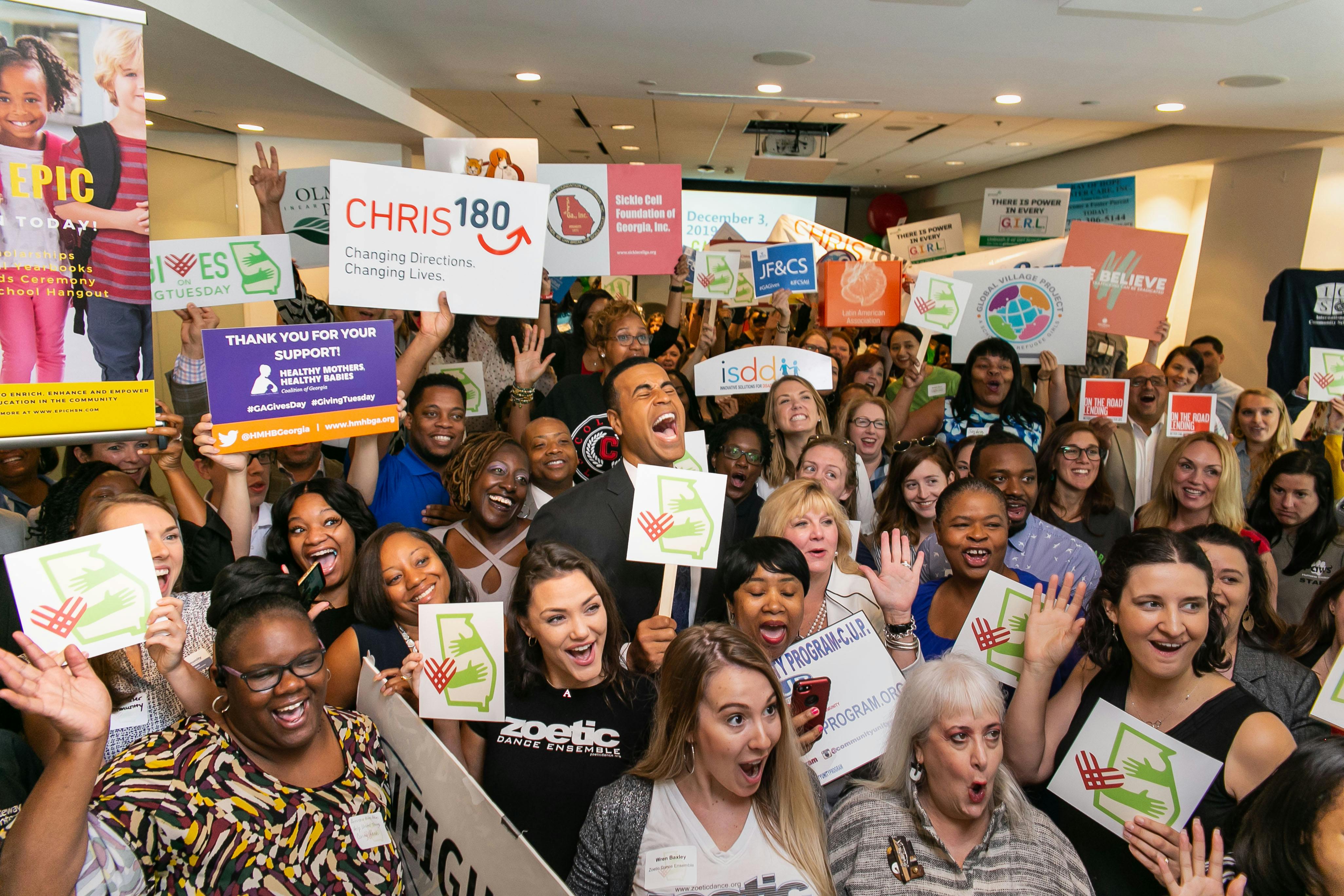 Giving Tuesday image with a happy crowd holding signs with the words and emblems for Giving Tuesday